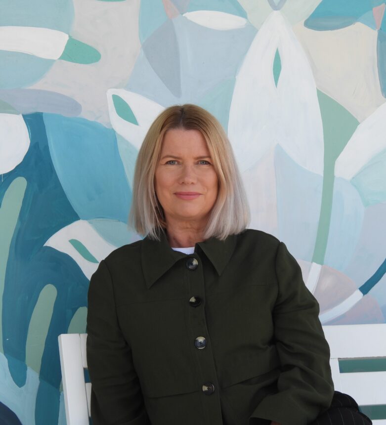 Image of a young woman sitting in from of a colourful wall.
